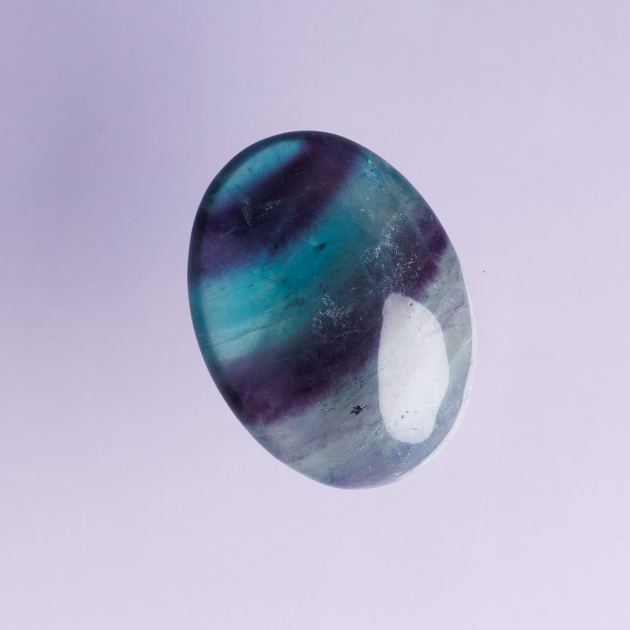 Oval-shaped gemstone with purple and green stripes on a light purple background