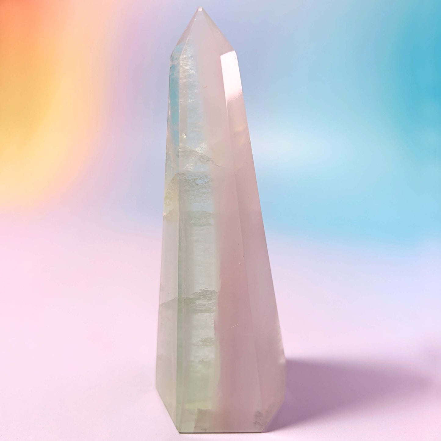 Yttrium Lavender Fluorite crystal obelisk tower on a rainbow gradient background, side view.