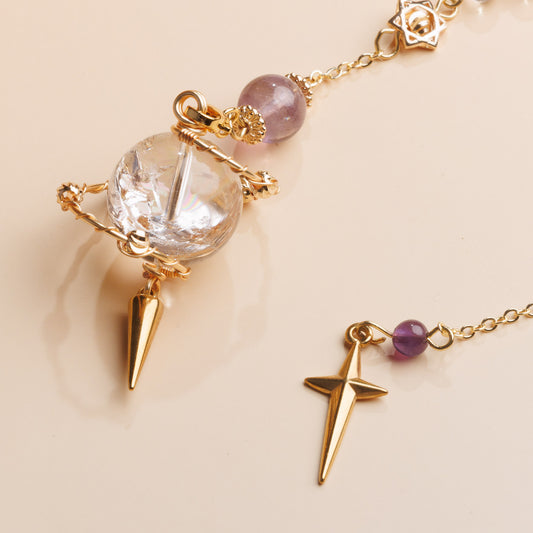Gold pendulum with crystal and star-shaped charms on a beige background