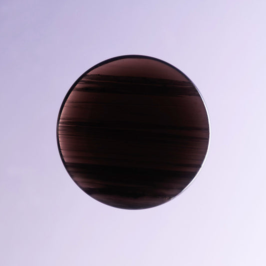 Circular midnight lace obsidian palmstone crystal on a light purple background.