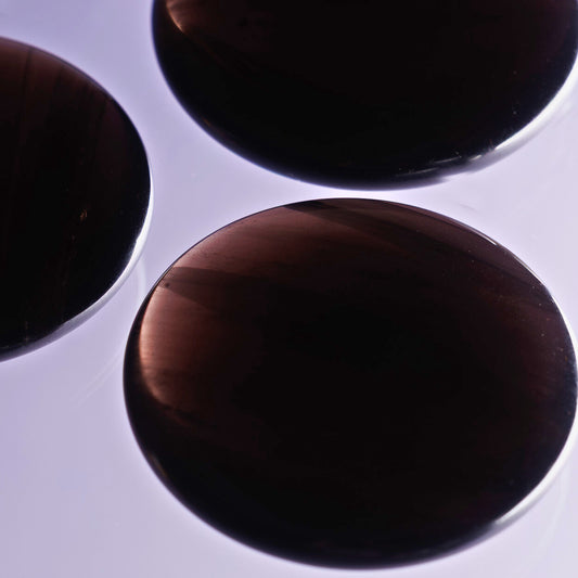 Three circular midnight lace obsidian palmstone crystals on a light purple background.
